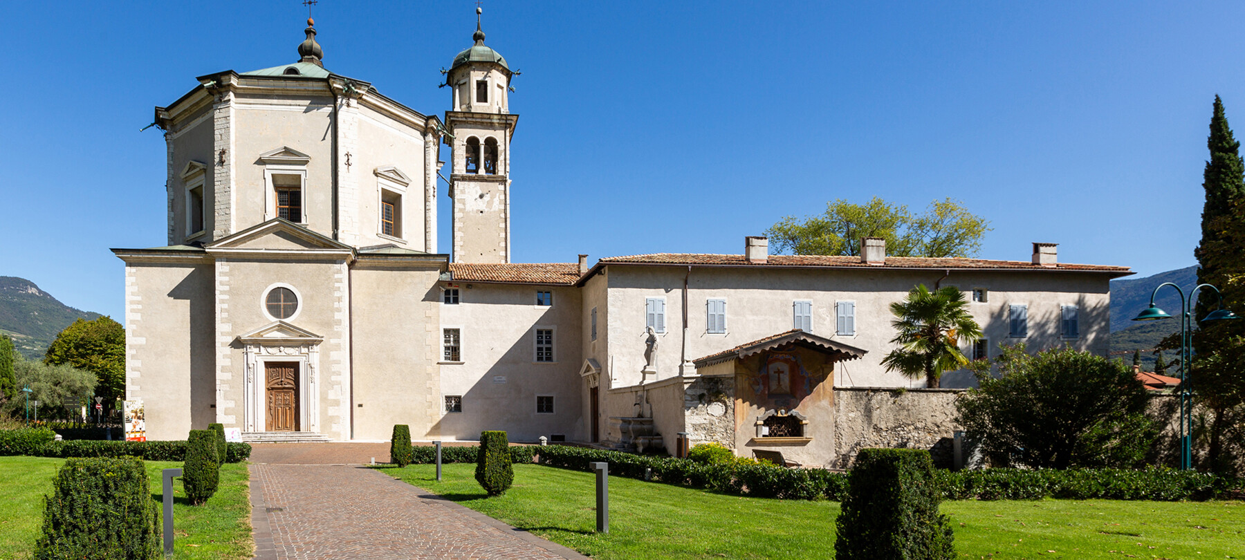 Chiesa dell’Inviolata, a Riva del Garda. L’esterno lineare, dalle geometrie pulite, nasconde un’anima barocca. Nella fotografia non ci sono persone. La porta della chiesa è chiusa. Tutto sembra silenzioso, in pace.