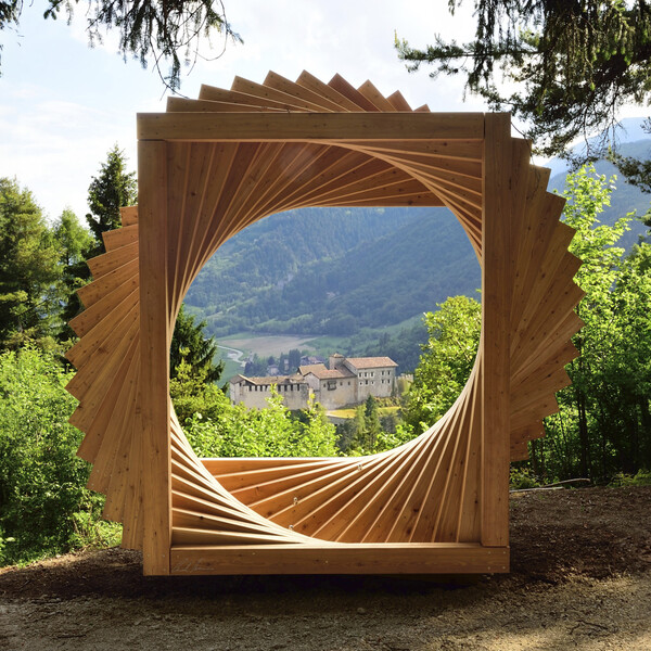 Bosco Arte Stenico, a work by Maurizio Corradi. The work, located at a panoramic point on the path, is a large spiral made up of wooden elements and looks like an open window on the panorama. In the centre, in the distance, is the castle of Stenico. Around the work, the trees of the forest.