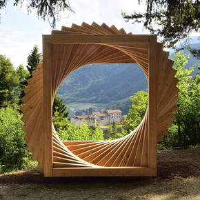 Bosco Arte Stenico, a work by Maurizio Corradi. The work, located at a panoramic point on the path, is a large spiral made up of wooden elements and looks like an open window on the panorama. In the centre, in the distance, is the castle of Stenico. Around the work, the trees of the forest.