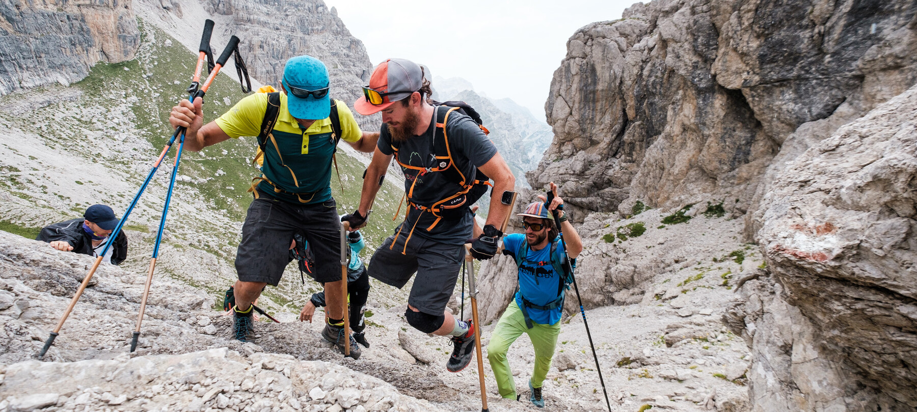 Nello scenario roccioso delle Dolomiti del Brenta, cinque alpinisti stanno raggiungendo una cima. È un gruppo composto da persone disabili e non. In primo piano, un ragazzo a cui manca la gamba destra affronta la salita con l’aiuto di un compagno di scalata e con speciali stampelle che gli permettono di sfruttare al meglio la forza delle braccia.
