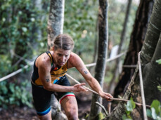 An X-Terra participant climbs up from a steep forest clinging to a rope.