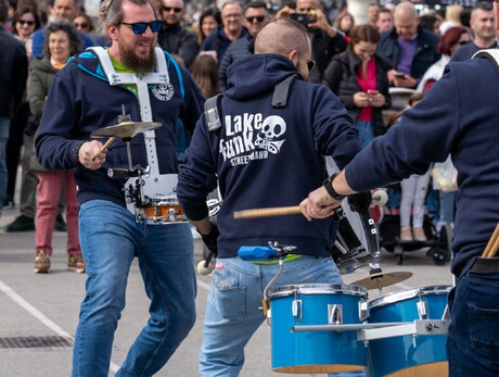 A GROUP OF DRUMMERS WITH DRUMS AND MANY SPECTATORS AROUND THEM WATCHING AND LISTENING