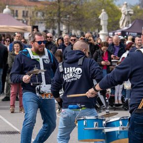 A GROUP OF DRUMMERS WITH DRUMS AND MANY SPECTATORS AROUND THEM WATCHING AND LISTENING