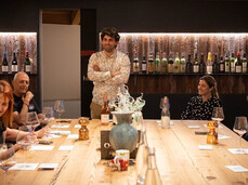 A group of people are seated at a table in the tasting room of a winery. They are enjoying themselves together with the winemaker, who is leading the tasting of his wines.