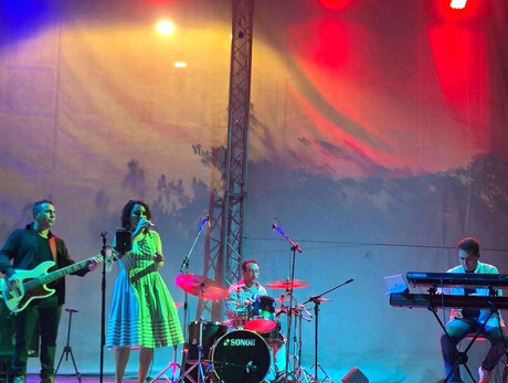 Three men playing instruments and one girl singing on stage with colorful lights