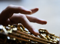 La foto inquadra una sezione di uno strumento a fiato e le dita del musicista mentre schiacciano i tasti dello strumento.