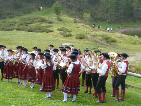 L'immagine mostra i componenti della banda con vestiti tradizionali mentre suonano all'aperto