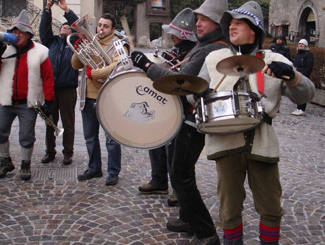 Nell'immagine si vedono i 5 componenti della banda intenti a suonare i loro strumenti in una piazza 