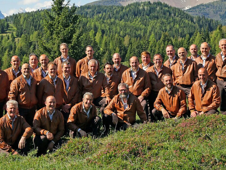 L'immagine mostra i componenti del coro in un prato all'aperto e sullo sfondo il monte Peller da cui il coro prende il nome