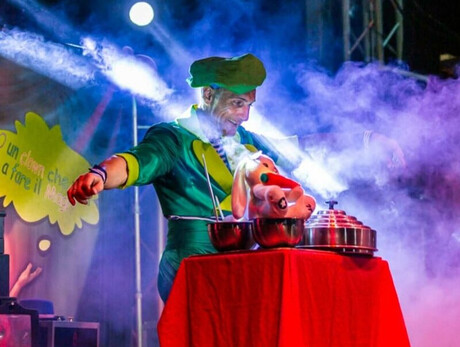 La foto mostra l'artista mentre si esibisce sul palco con un numero di magia per bambini