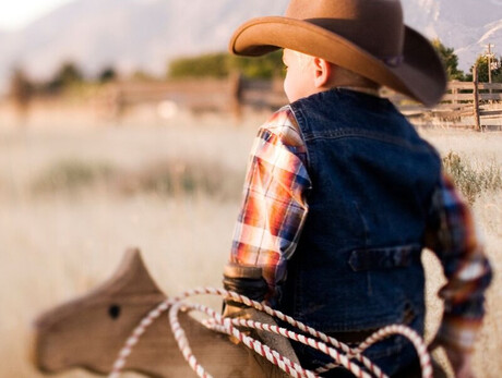 L'immagine mostra un bambino vestito da cowboy; con sè ha anche una corda e un cavallo di legno