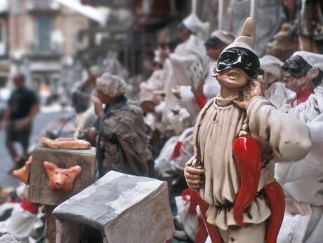 Nell'immagine si vede una strada di Napoli dove vendono statutte di pulcinella e cornetti di peperoncino