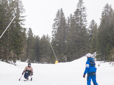 Under a grey winter sky, a ski instructor gives a lesson to a person with a disability on the monoski.