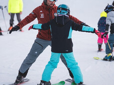 During an inclusive ski lesson on the snow of Paganella, an instructor helps a child find their balance on skis.