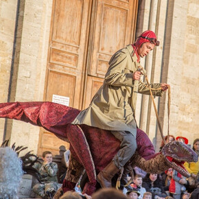 A boy wearing a red cap on his head riding a puppet dinosaur.