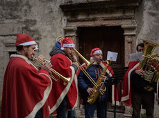 L'immagine ritrae 4 uomini vestiti con cappello e mantello di Babbo Natale suonano trombe e tromboni intonando canti natalizi