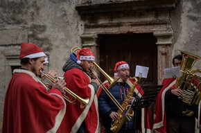L'immagine ritrae 4 uomini vestiti con cappello e mantello di Babbo Natale suonano trombe e tromboni intonando canti natalizi
